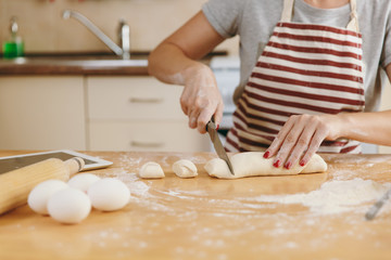 Obraz na płótnie Canvas A young woman sitting at a table with tablet, cuts a dough with a knife into pieces and going to prepare a Christmas cakes in the kitchen. Cooking home. Prepare food close up.