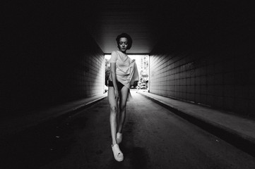 Fototapeta premium young woman with bare legs dressed in white sneakers and a long T-shirt, against the backdrop of cityscapes. street fashion, black and white style
