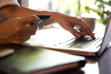 Naklejka premium Hands holding credit card and using laptop. On-line shopping, Travel booking concept. Selective focus.