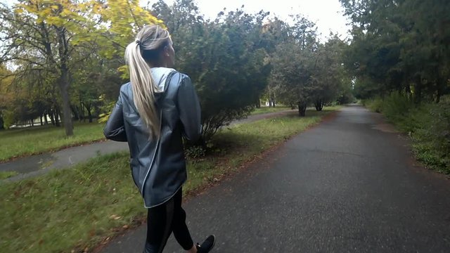Beautiful young blonde girl is running in park at rainy day, doing sports, a healthy lifestyle.. Slow motion.