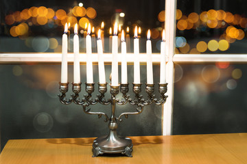 Happy Hanukkah. Low key image of jewish holiday Hanukkah with menorah by the window with the night view out of focus on Tel Aviv, Israel