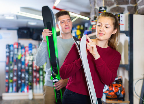 Salesman is helping woman in ski equipment to choose ski in sport store.