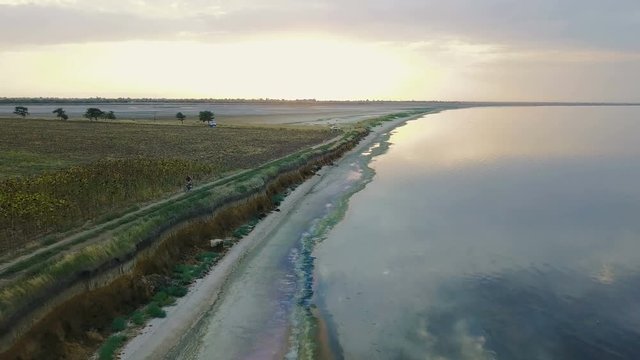 aerial footage of man riding a bicycle near the beautiful lake during sunset