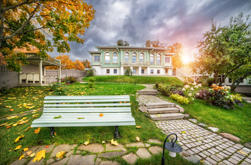 Скамеечка в осеннем саду A bench in an autumn garden and a house