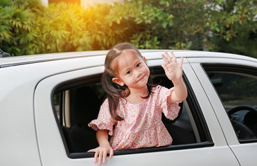 Fototapeta premium Adorable asian little girl in car smiling and looking camera sitting on a backseat of a car waving goodbye.