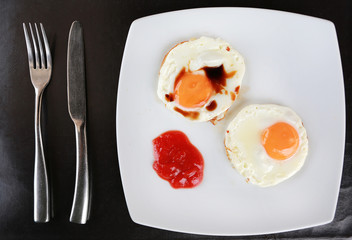 Fried egg with tomato sauce on white plate with fork and knife on the table.