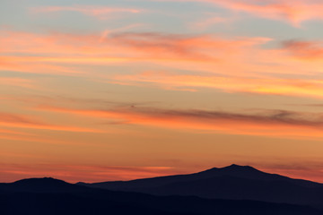 Fototapeta na wymiar A silhouette of a mountain peak at sunset, under a big sky with beautiful, striped red clouds