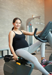 Plakat Sporty pregnant woman exercising in fitness room with smiling and looking at camera.