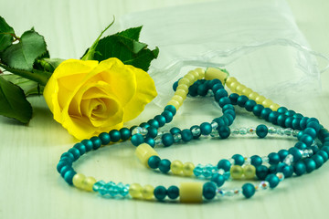 A yellow rose on a wooden table with a necklace