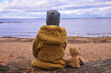 Little girl with toy Teddy bear sits on the shore of the sea