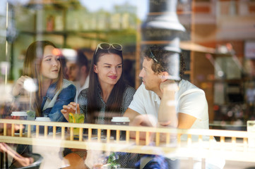 Three young friends behind glass of cafe.