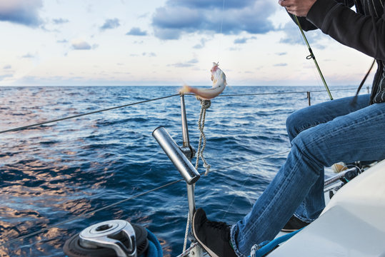 A man catching a fish from the yacht. Sunset fishing.