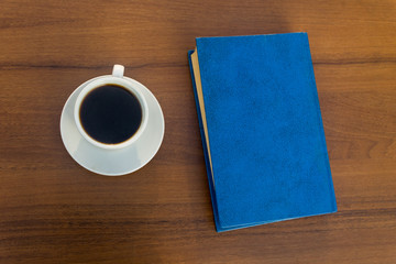 Cup of coffee and closed book on wooden table