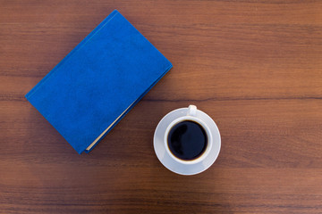 Cup of coffee and closed book on wooden table