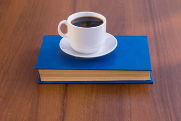 Cup of coffee and book on wooden table