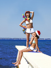 Portrait beautiful women, has haired long hair, blue and white bikini, sunglasses, slim body, happy smile face, red Christmas hat. Tropical hot sea. Having fun together.