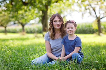 Beautiful young mother and little daughter sitting on green grass and resting