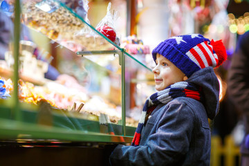 Little kid boy with gingerbread and sweets stand on Christmas market