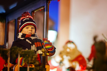 Little kid boy on carousel at Christmas market