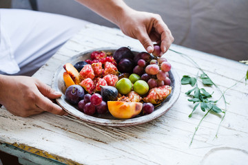 Person serving eating grape on tray full of fresh seasonal fruits
