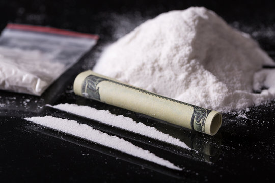 Rolled hundred dollars banknote, two lines and pile of cocaine on black background