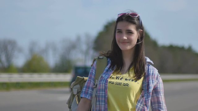 Young hitchhiker shows thumb up stands near the road