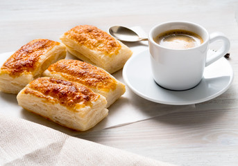 morning Breakfast with fresh rolls of puff pastry and Cup of coffee on white wooden table. Side view, the light of day.