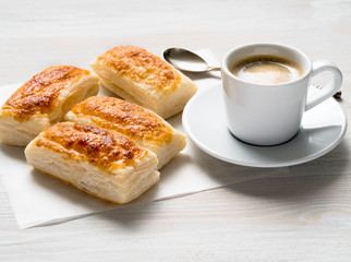 morning Breakfast with fresh rolls of puff pastry and Cup of coffee on white wooden table. Side view, the light of day.