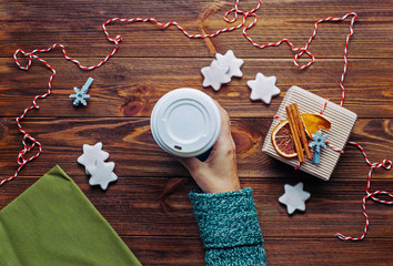 Female hand holding cup with coffee with marshmallow on rustic wooden background