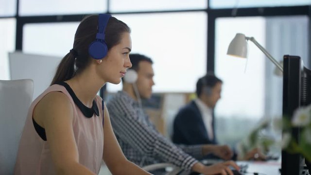 Cheerful customer support team with headphones working at computers & chatting
