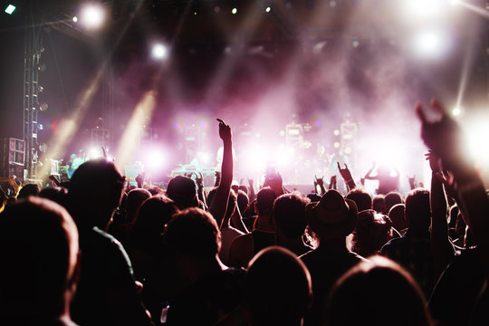 silhouettes of concert crowd and mohawk punk hair style in front of bright stage lights