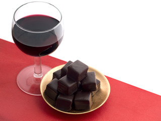 Red wine and dark chocolates on red cloth. With copy space.