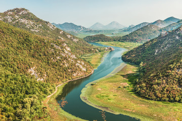 Fototapeta na wymiar Scenic magnificent view of the winding Crnojevica river behind the green mountains in the National Park of Lake Skadar, Montenegro, the natural landscape.