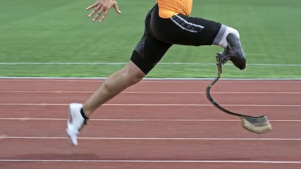 Slow mo side view of amputee athlete with prosthetic blade running on stadium track outdoors - Powered by Adobe