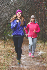 A healthy way of life. Two girls girlfriends of athletes running in the woods with a smile looking