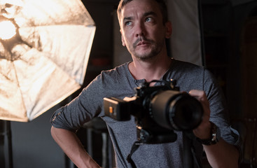 A serious photographer with a camera on the background of lighting equipment
