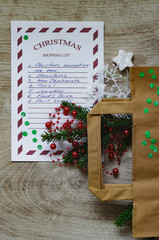 Christmas shopping list with spruce branch, white snowflake, silver star, eco paper shopping bag, ornaments and green confetti.