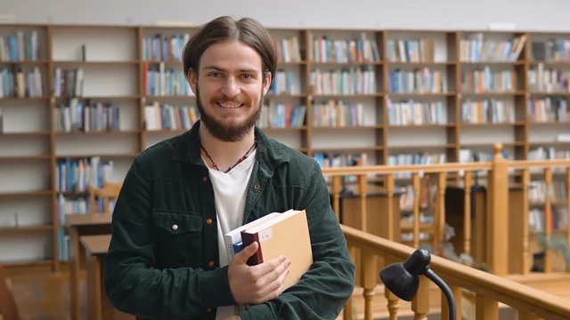 Portrait of handsome long hair student man in library hall with bookshelves