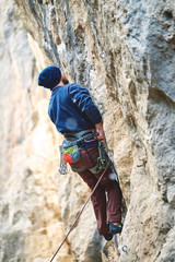 Fototapeta premium male rock climber climbs on a rocky wall at winter sunny day. Man climber in warm clothes on yellow cliff.
