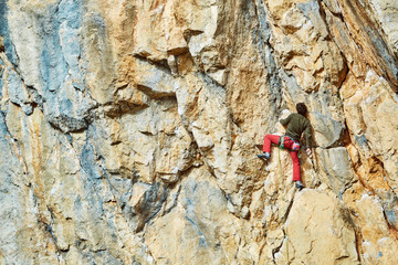 Fototapeta premium male rock climber climbs on a rocky wall at winter sunny day. Man climber in warm clothes on yellow cliff.