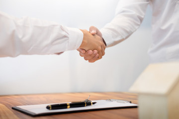 Estate agent shaking hands with customer after contract signature as successful agreement in real estate agency office. Concept of housing purchase and insurance