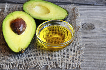 Avocado oil in a glass bowl and fresh organic avocado on old wooden background.Healthy eating,diet,body care concept. © svf74