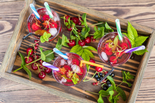 Three glasses of refreshing drink flavored with fresh fruit in wooden box surrounded by fruit. Top view. Wooden background