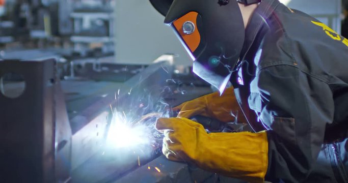 Cinemagraph of factory worker in protective mask welding metal material with torch; sparks flying around flame