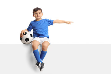 Little footballer sitting on a panel and pointing