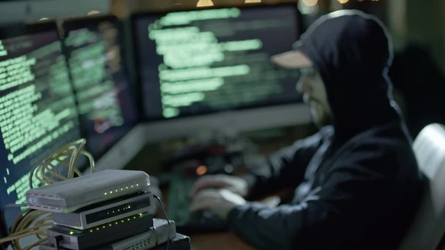 Cinemagraph of hacker typing programming code at computer workstation in dark office