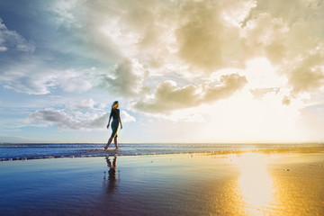 Young woman walking on the beach at sunset. Sky is cloudy and beautiful.