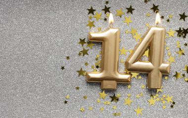 Number 14 gold celebration candle on star and glitter background
