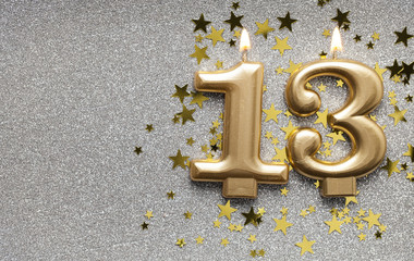 Number 13 gold celebration candle on star and glitter background