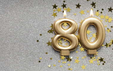 Number 80 gold celebration candle on star and glitter background